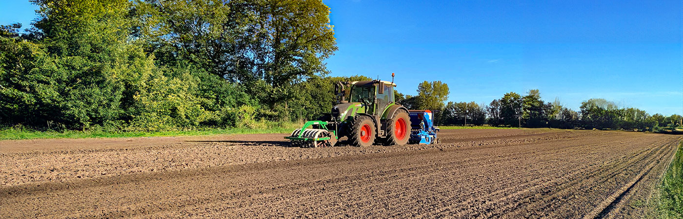 Traktor bei Feldarbeit der Erde grubbert und im Sonnenschein mit blauem Himmel agiert. Bäume im Hintergrund