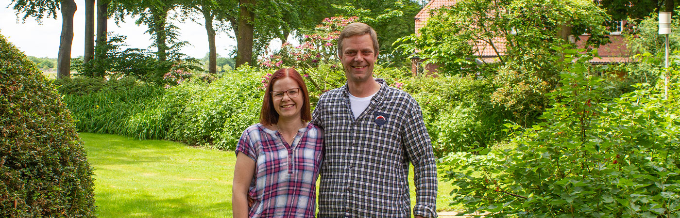 Portraitbild Christian und Stefanie Kleine-Dütting im Garten mit blühednen Büschen im Hintergrund